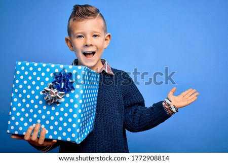 Young little caucasian kid holding surprise box as birthday or Christmas present very happy and excited, winner expression celebrating victory screaming with big smile and raised hands
