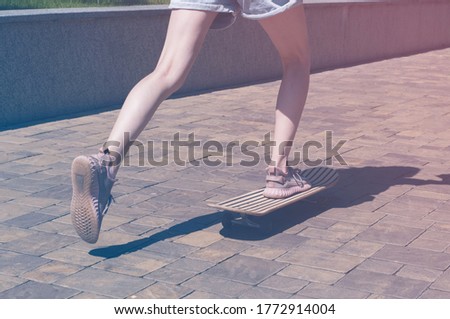 Teen girl rides on a skateboard in city park. Female legs in sneakers closeup. Bright vintage photo