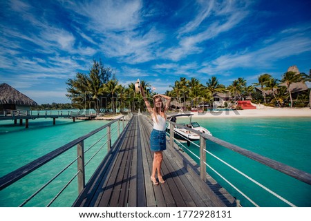 beautiful blonde girl  posing on dock, tropical resort in background