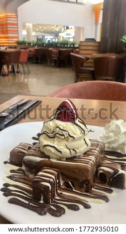 A Picture a delicious dessert consisting of brownies cake with vanilla ice cream ball sprinkled with fun chocolate sauce.
