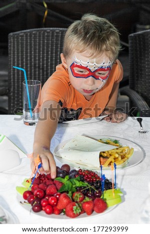 Young boy with painted face reaching for fruit