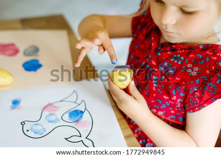little toddler girl painting with finger colors and potato stamp during pandemic coronavirus quarantine disease. Happy creative child, homeschooling with parents