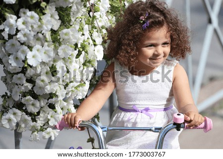 little girl with a bicycle on a city street with flowers. High quality photo