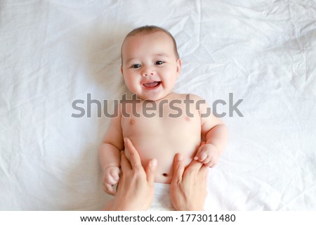 Adorable newborn baby boy with smiling face top view relaxing time doing belly massage by his mother. Mixed race Asian-German infant massaging and laughing. Royalty-Free Stock Photo #1773011480