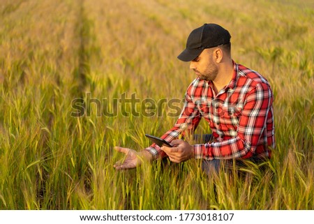 Young farmer standing in filed of wheat. Tablet in his hand and taking pictures of crops. Inspecting crops