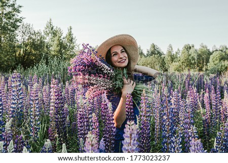 Girl in the lupine field. Brunette in a hat and blue with a bouquet of lupins