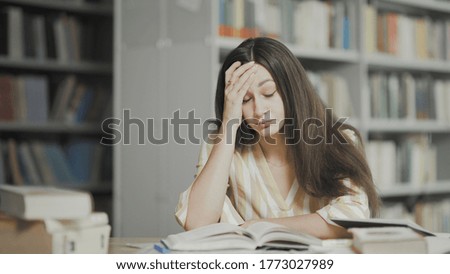 Tired young woman is preparing for examination at university library