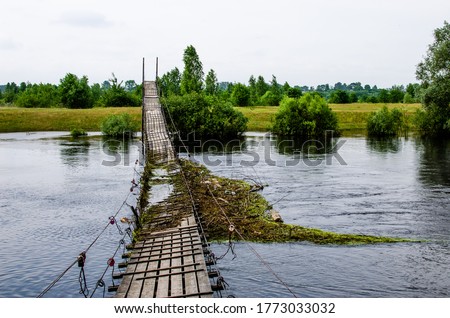 Suspension bridge over the river is broken and flooded against the backdrop of a summer landscape Royalty-Free Stock Photo #1773033032