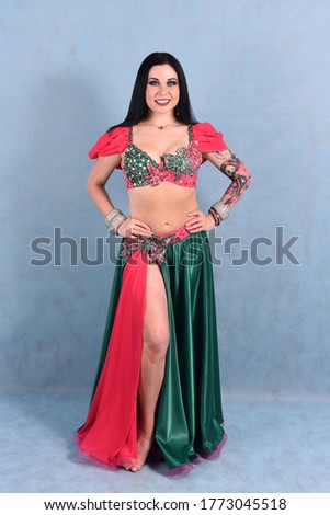A beautiful Oriental dancer poses with a beautiful smile in the Studio on a blue background in a pink and green suit