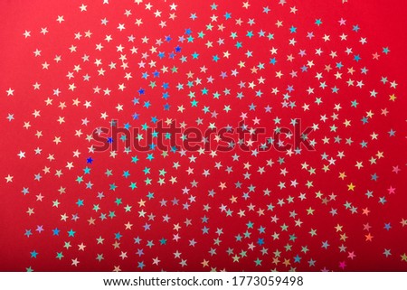 Colorful, shiny confetti on a red background. Christmas, holiday, or party background. The concept of the celebration. Top view, flat lay. Festive holiday confetti.