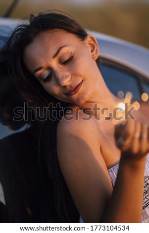 A vertical shallow focus shot of young caucasian female posing with Bengal light on a car background