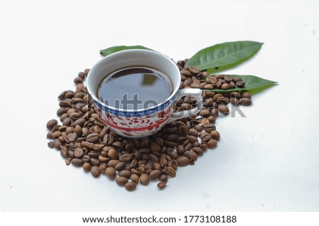 a cup of coffee with coffee seeds and green leaf isolated at white background.