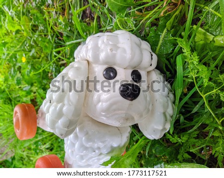 old and plastic toy in the form of a white poodle on the grass