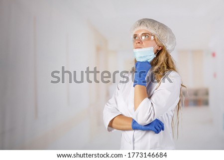 Doctor a woman in a protective suit stands thoughtfully in the hospital corridor. Coronavirus infection is life-threatening