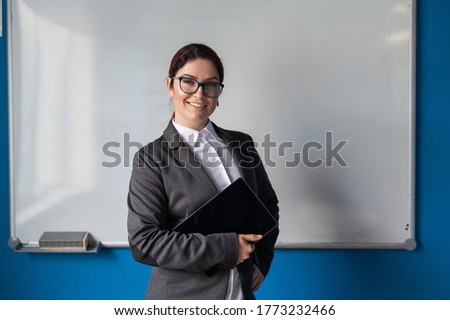 Beautiful woman in a suit with a digital tablet in her hands. A smiling female business coach with glasses stands in a conference room near a white board. Workshop at the office. Royalty-Free Stock Photo #1773232466