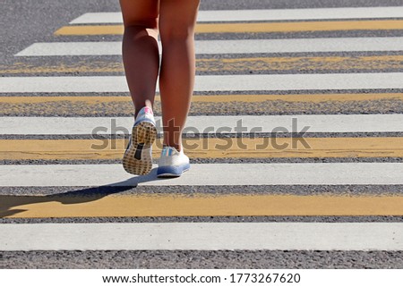 Girl crossing the street, female legs in sneakers on pedestrian crossing. Concept of road safety, woman in summer city