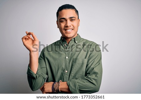 Young brazilian man wearing casual shirt standing over isolated white background with a big smile on face, pointing with hand and finger to the side looking at the camera.