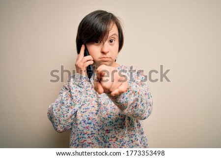 Young down syndrome woman having a conversation speaking on smartphone pointing with finger to the camera and to you, hand sign, positive and confident gesture from the front