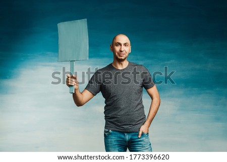 Attractive bald man in a T-shirt with a protest poster in his hands on a blue background.