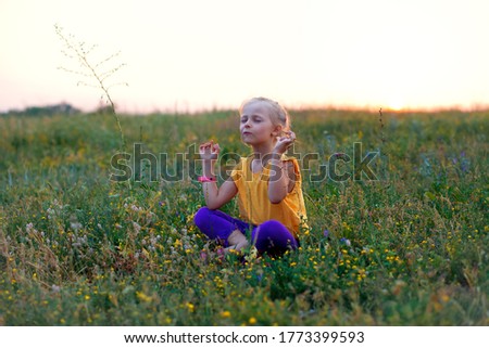 A child sits in a field at sunset in summer. Summer outdoor recreation. Meditation in the fresh air. Children's yoga and meditation. Psychological health