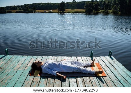 a young girl does yoga on a lake on a Sunny summer day, meditation, relaxation pose, Shavasana or dead man's pose, retreat in nature, peace, relaxation Royalty-Free Stock Photo #1773402293