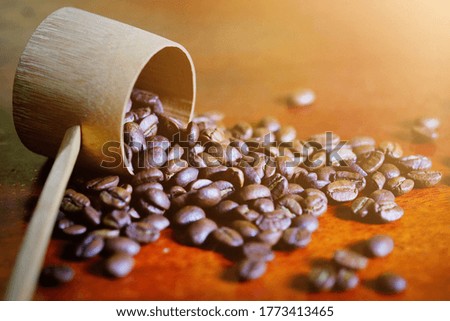 These coffee beans with a bamboo ladle resting on a warm light brown wooden table.