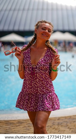 Portrait of beautiful smiling young woman with red glasses in hand on background of water park.