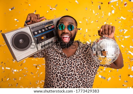 Close-up portrait of his he nice handsome bearded cheerful cheery cool emotional guy holding in hands shine disco ball carrying player isolated on bright vivid shine vibrant yellow color background
