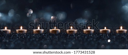 Candlelights in the darkness with blurred golden bokeh. Horizontal background with short depth of field for religious rituals and spiritual meditation or grief.
