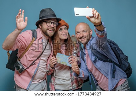 Three happy friends of tourists with backpacks travel and take pictures on a smartphone.