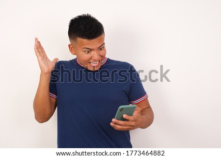 Young handsome hispanic man wearing casual t-shirt standing over white isolated background holding in hands cell reading browsing news 