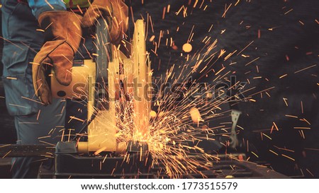 Defocus fire spark while Industrial technician engineer in blue protective cloth wear safety mask, cutting steel structue. professional technical man cut steel structure with fire spark in factory.