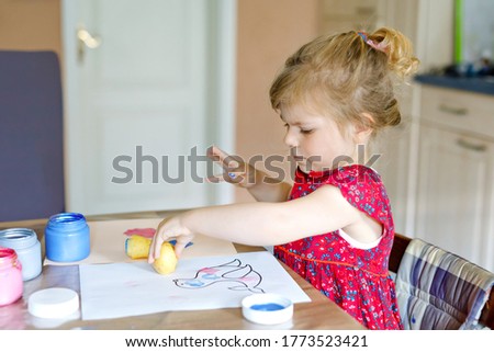 little toddler girl painting with finger colors and potato stamp during pandemic coronavirus quarantine disease. Happy creative child, homeschooling with parents.