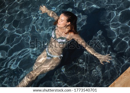 Caucasian woman spending time by swimming pool self isolating, relaxing in water in a swimming pool. Social distancing in quarantine lockdown during coronavirus covid 19 epidemic.