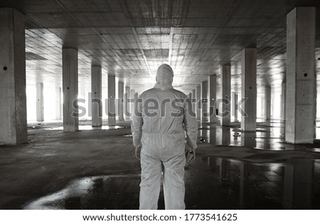 Rear shot of a Person Dressed in White single use disposable Jumpsuit holding a Spray Can looking down an abandoned Factory