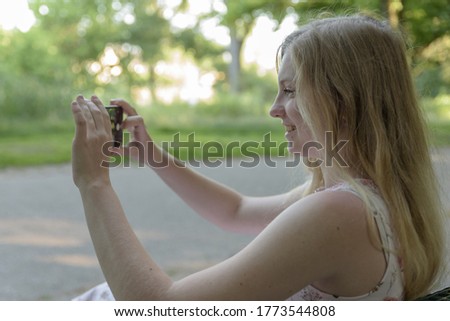 A young woman is sitting in the park and taking pictures with cellphone