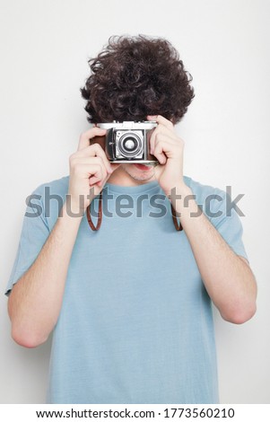 laughing haired guy with retro camera on his face taking a picture on white background