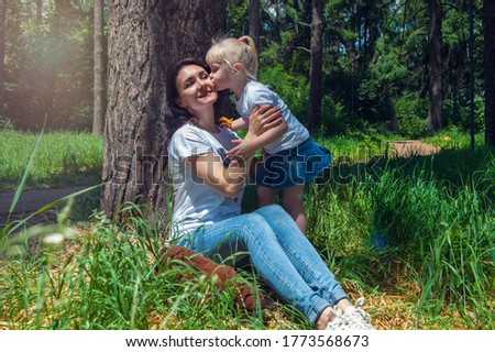 Mother with daughter resting in the park on the grass. Small girl kissing her mom 