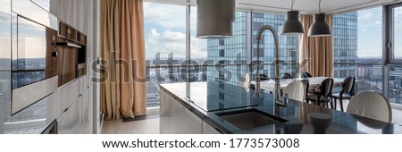 Open kitchen with black countertop, white cupboards and big windows and city view Royalty-Free Stock Photo #1773573008