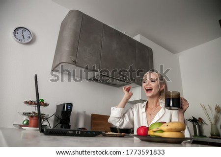 Girl working on laptop in kitchen at home and very emotional. Woman gestures with hands. Business from home. Cute Slavic woman in kitchen looks at computer. Emotions female. Concept of homework
