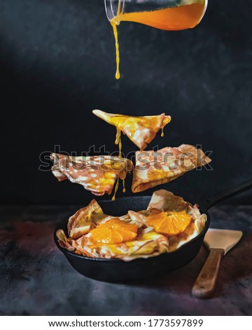 Selective focus, Crepes with Orange Sauce in black pan, dark background. Levitation food photography. Traditional French crepe Suzette with fresh orange sauce. Copy space. Conceptual food image. Royalty-Free Stock Photo #1773597899