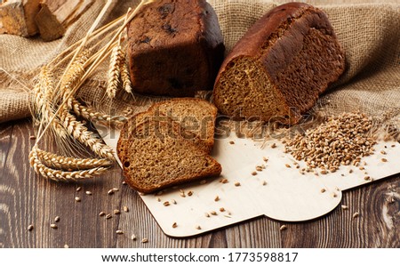 Bread in form of triangle and with sunflower seeds near spikelets of wheat lies on old weathered wooden table. Rustic bread and wheat on an old vintage planked wood table. Free text space.