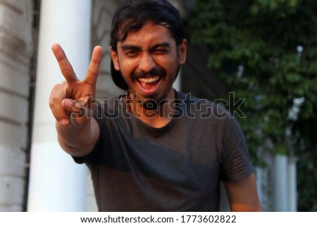 Young Man winking and smiling while showing peace sign with his fingers.