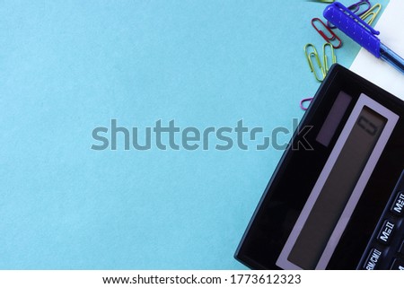 Large black calculator with blue pen and paper clips on a light green background. Conceptual photo of calculations, accounting, profit, loss, tax with place for text