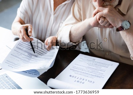 Cropped view of senior woman pointing at papers near husband and document with debt collection lettering on table Royalty-Free Stock Photo #1773636959