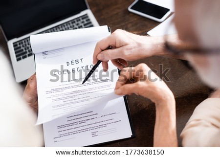 Selective focus of senior man holding pen near wife with debt collection lettering on papers Royalty-Free Stock Photo #1773638150