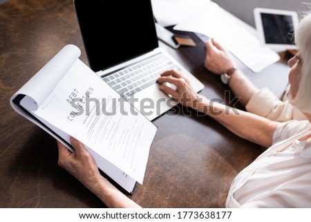 Selective focus of woman using laptop and holding papers with debt collection lettering near man at table Royalty-Free Stock Photo #1773638177
