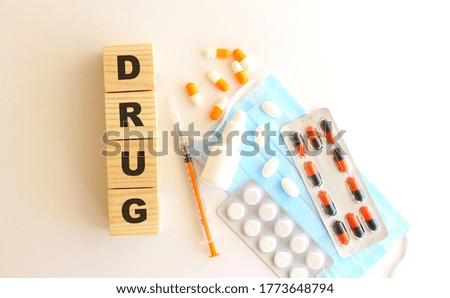 The words DRUG is made of wooden cubes on a white background with medical drugs and medical mask. Medical concept.