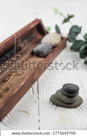 Pyramids of gray zen pebble stones with green leaves and incense stick on white wooden background. Concept of harmony, balance and meditation, spa, massage, relax