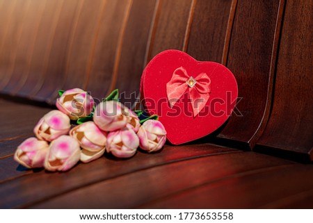 Picture of heart shape box and tulips on the wooden bench on sunny day.